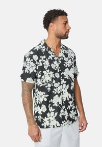 Chemise noire à manches courtes avec des motifs floraux de roses blanches, col à bouton, coupe décontractée et texture de tissu douce.