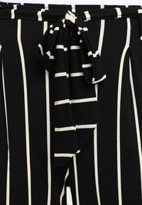 Pantalons rayés noir et blanc en tissu texturé, avec une taille à nouer et des rayures verticales de largeurs variées.