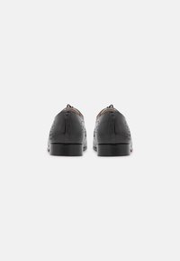 Scarpe in pelle nera con dettagli perforati, punta arrotondata e tacco basso e solido. Accenti cuciti sulla parte superiore e finitura liscia.