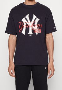 Svart bomullströja med en vit och röd New York Yankees-logotyp där "Bronx, NY" och "Etablerad 1903" är tryckt på framsidan.