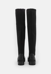 Botas negras hasta la rodilla con un upper de textil suave y una suela de goma gruesa. Presentan un ribete acanalado en la parte superior para un ajuste seguro.