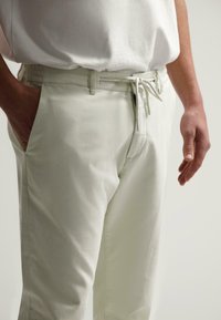 Pantalons beige clair avec taille élastique et cordon de serrage, en tissu lisse et texturé, avec poches latérales et coupe décontractée.