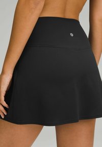 Black athletic skirt with a high waistband, made of smooth, stretchy fabric. Simple hem design, featuring subtle stitching and brand logo.