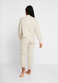 Beige Sweatshirt und passende Jogginghosen aus weichem Stoff. Der Sweatshirt hat einen gerippten Saum und Bündchen; die Hose hat elastische Knöchel und Taschen.
