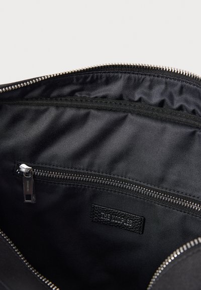 Melnas somas iekšpuse ar gludu audumu, nodalījumu ar rāvējslēdzēju un ādas etiķeti ar zīmola nosaukumu. Malai ir sudraba metāla rāvējslēdzēja detaļas.