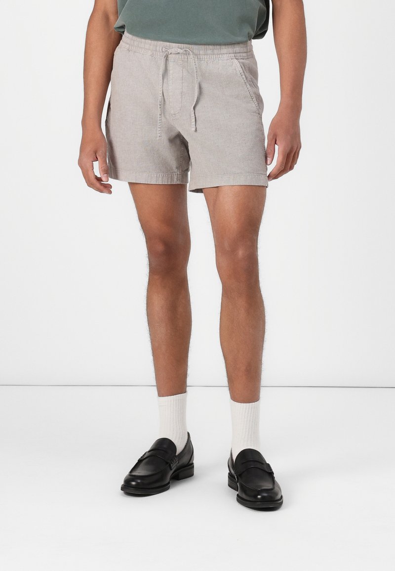Shorts en lin gris avec une taille élastique et un cordon de serrage, associés à un haut vert, des mocassins noirs et des chaussettes blanches mi-mollet.