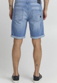 Lyseblå denimshorts med oppbrettede kanter, fem lommer og kontrastbroderi. Bakdelen har merkevareklistre og lett slitasje.