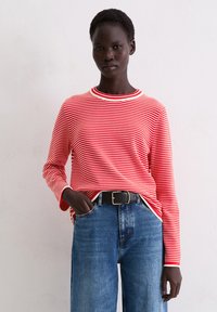 Rot-weißt gestreiftes Langarmoberteil mit Rundhalsausschnitt, kombiniert mit hochgeschnittenen blauen Jeans und einem schwarzen Gürtel.