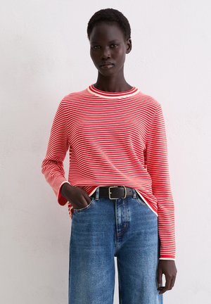 Rot-weißt gestreiftes Langarmoberteil mit Rundhalsausschnitt, kombiniert mit hochgeschnittenen blauen Jeans und einem schwarzen Gürtel.