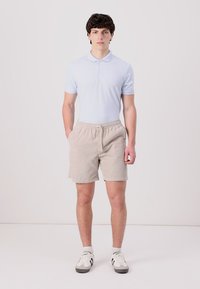 Camiseta polo de color azul claro con mangas cortas, combinada con pantalones cortos beis a rayas y zapatillas blancas con detalles en negro. Un atuendo simple y casual.