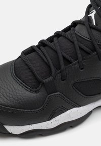 Černá sportovní obuv s texturovaným koženým svrškem, síťovinovými detaily a černými tkaničkami. Obsahuje bílou tečkovanou mezipodešev a černou gumovou podrážku.