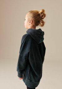 Hoodie noir surdimensionné avec une finition texturée, dotée d'une grande capuche et de poignets côtelés, vue de l'arrière sur un fond neutre.