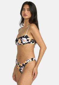 Svart blommig bikini-set med ljuslila remmar, stora persiko- och rosa blommönster på slätt tyg, med högskurna underdelar.