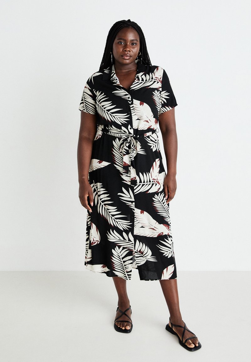Black button-up dress with short sleeves, featuring white and red leaf patterns, a cinched waist with a tie, and a mid-calf length. Black sandals.