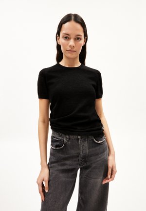 Schwarzes T-Shirt mit kurzen Ärmeln aus weichem Material und rundem Ausschnitt. Kombiniert mit hoch geschnittenen, ausgebleichten schwarzen Jeans mit Distressed-Details.