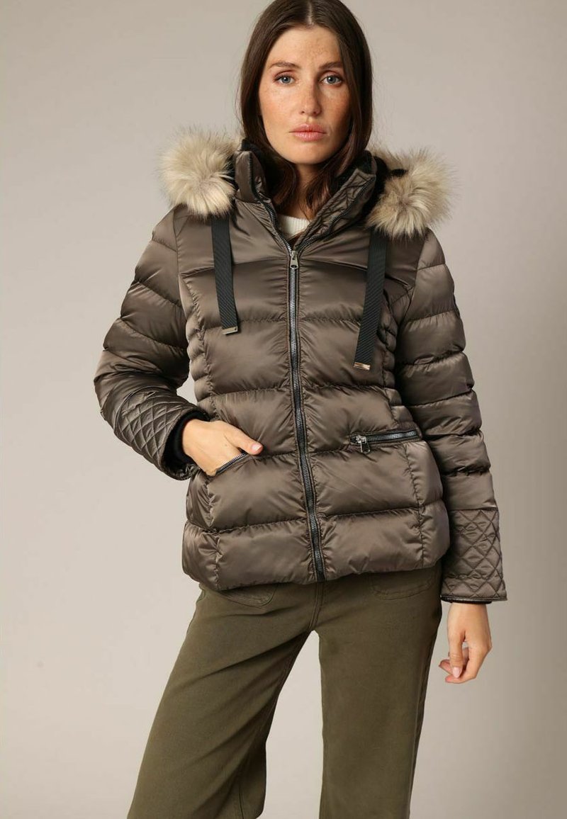 Veste marron rembourrée avec capuche en fourrure, cordons de serrage noirs, poches zippées et détails matelassés sur les manches. Matériau doux et brillant.