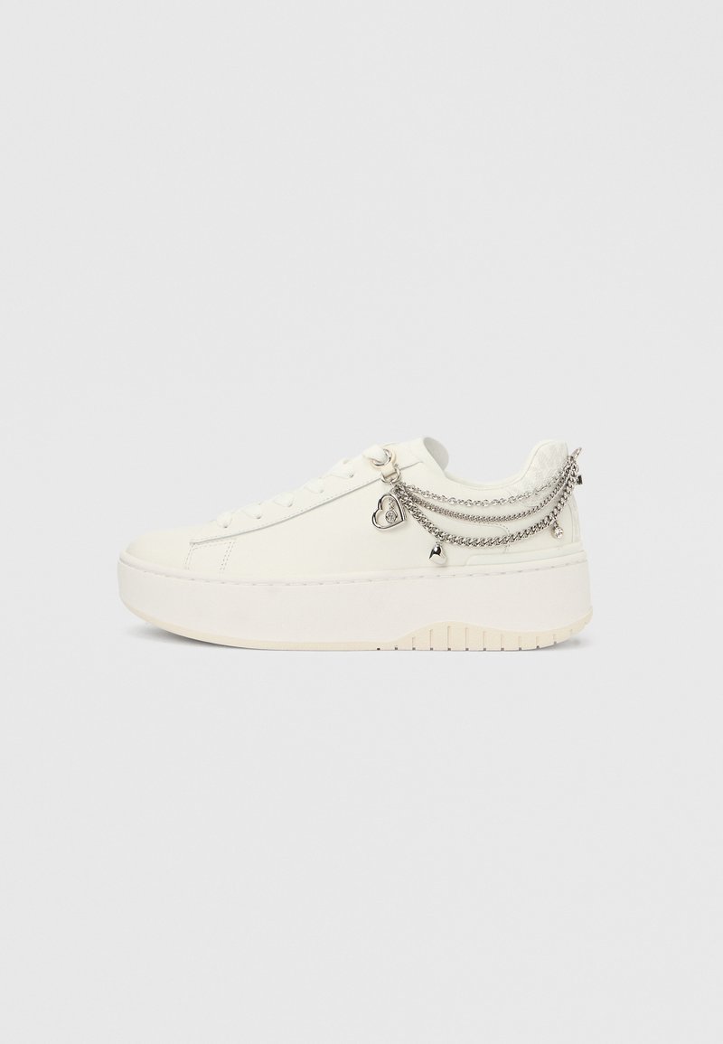 Λευκό πλατφόρμα αθλητικό παπούτσι με ασημένια αλυσιδάκια, που περιλαμβάνουν καρδούλες και καμπανάκια, προσαρτημένα κοντά στον αστράγαλο, σε απλό φόντο.