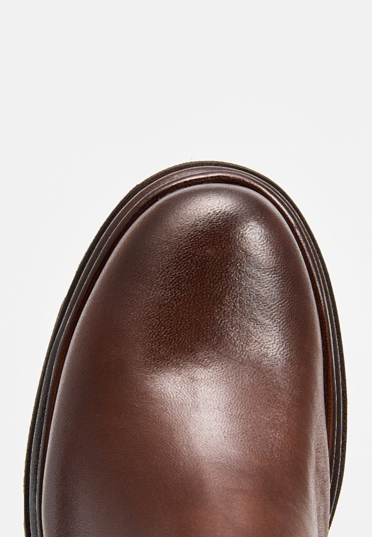 Scarpa di pelle marrone con una superficie liscia, punta rotonda e suola stratificata con dettagli di cucitura discreti.