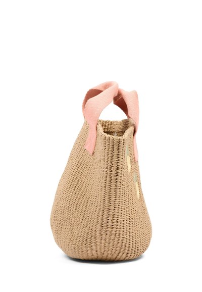 Beżowa torba typu tote z plecionego słomy z szerokimi różowymi tkaninowymi uchwytami, stojąca pionowo na białym tle.