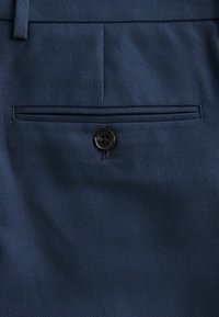 Pantalones de tela azul marino con un bolsillo trasero con un botón negro redondo. Material texturizado con un patrón sutil. Diseño ajustado.