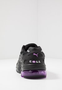 Svart idrottssko med ovandel av mesh och syntetmaterial, lila detaljer och en tjock, genomskinlig lila sula. Har "CELL"-logotypen på baksidan.