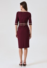 Abito aderente bordeaux con maniche a tre quarti, strisce orizzontali beige, zip sul retro e orlo a ginocchio. Tessuto dalla consistenza liscia.