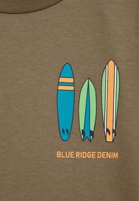Alyvuogių spalvos marškiniai su trimis stilizuotais banglentių piešiniais mėlyna, žalia ir oranžine spalvomis, su juodais kontūrais. Tekstas skaito "BLUE RIDGE DENIM" oranžine spalva.