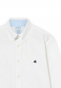 Biała koszula zapinana na guziki z jasnoniebieskim wykończeniem kołnierza oraz małym granatowym logo niedźwiedzia na lewej piersi. Standardowy krój, materiał bawełniany.