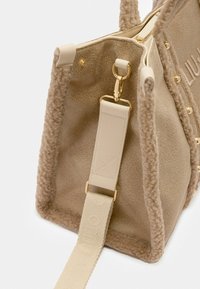 Beige bag made of textured material with a fuzzy trim. Features gold-tone hardware and a detachable strap with embossed detailing.