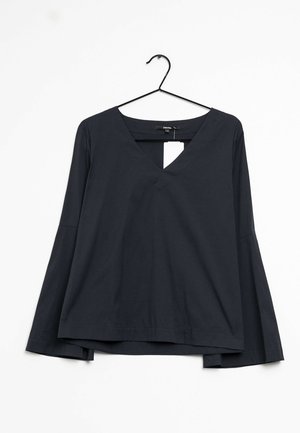 Sort bluse med lange ærmer og V-hals, hængende på en sort bøjle mod en hvid baggrund med en synlig hvid prisseddel.