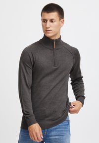 Mørkegrå zip-sweater med høy krage, ribbestrikkede mansjetter og nederkant, samt et strukturert strikkemønster.