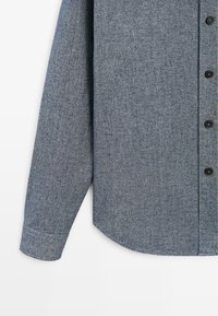 Grijze, gestructureerde langemouwen shirt met een ronde zoom, voorzien van zwarte knopen en een gedeeltelijk zichtbare manchette.