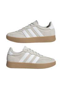 Zapatillas Adidas con un upper de ante beige, acentos de cuero blanco, tres franjas blancas y una suela de goma para tracción.