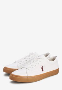 Zapatillas de lona blancas con una suela de goma texturizada, que presentan un logo de langosta en color burdeos en el lateral y un diseño clásico de cordones.