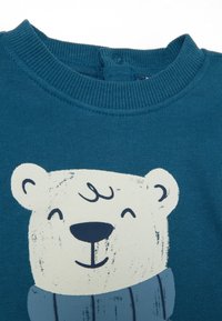 Sudadera verde azulado con cuello de canalé; presenta un diseño impreso de un oso polar con una expresión sonriente y una bufanda azul. Textura de algodón suave.