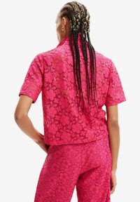 Lace todel i lys pink med blomster mønstre, kortærmet top og tætsiddende bukser. Let, tekstureret stof med åben vævning.