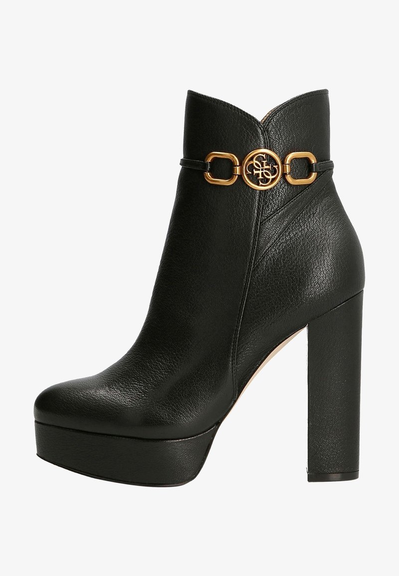 Bottine en cuir noir avec talon haut à bloc, semelle plateforme et boucle décorative dorée autour de la cheville.