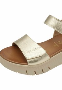 Gouden, gestructureerde synthetische sandalen met twee brede banden. Dikke witte zool met uitgesproken profielontwerp. Bruine binnenzool zichtbaar.