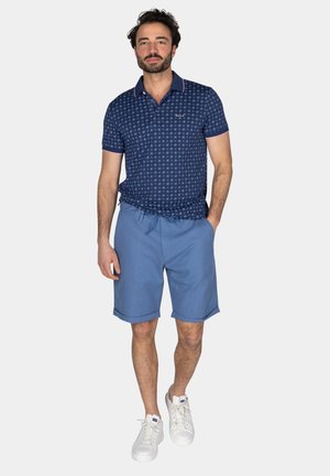 Marineblauw geblokt poloshirt met een kraag en korte mouwen, gecombineerd met lichtblauwe shorts en witte sneakers. Casual zomerlook.