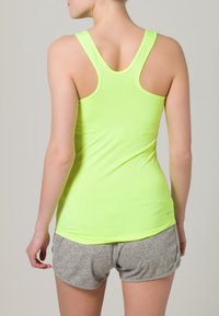 Neonowo zielony top na ramiączkach typu racerback, wykonany z elastycznej tkaniny, w zestawie z szarymi spodenkami sportowymi. Gładka tekstura i dopasowany fason.