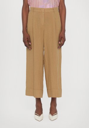 Braune, weite Hosen mit strukturiertem Finish, hohem Bund und Falten-Details. Der Saum ist umgeschlagen, um zusätzliche Dimension zu verleihen.
