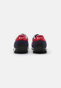 Sneaker blu navy con accenti rossi, dotate di un tallone posteriore testurizzato e suola in gomma con motivi di trazione a forma di stella. Logo ben visibile.