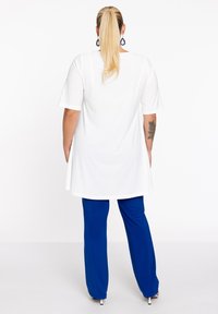 T-shirt blanche surdimensionnée à manches courtes, avec un ourlet arrondi, associée à un pantalon bleu ample. Tissu lisse, design simple, sans motifs ni accents.