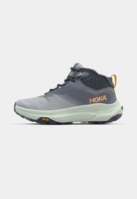 Pelēki HOKA pārgājienu zābaki ar teksturētu virsu, sintētiskiem akcentiem un gaiši zaļu vidusslāni. Iezīme ir Vibram zole, kas nodrošina saķeri.