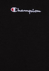 Camiseta de algodón negra con textura suave, que presenta un logotipo "Champion" bordado en blanco y un acento rojo en la "C". Diseño simple y elegante.