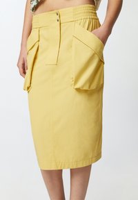 Žuta pamučna suknja s elastikom u struku, prednjim kopčanjem na dugmad i velikim bočnim dzepovima za dodatnu funkcionalnost.