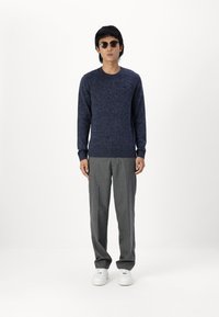 Jersey de lana de color azul marino con cuello redondo, combinado con pantalones gris claro y zapatillas blancas. Los accesorios incluyen gafas de sol redondas.
