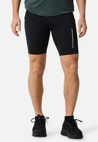 Pantaloni sportivi neri realizzati in materiale elastico, con un design aderente, una striscia riflettente sul lato e una texture liscia.