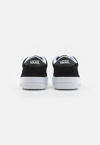 Schwarze Wildleder Vans-Schuhe mit weißen Gummisohlen und einem gepolsterten Kragen. Die Rückseite ist mit einem schwarzen Logo-Etikett auf einer strukturierten Oberfläche versehen.