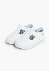 Scarpe da ginnastica bianche con forma arrotondata, caratterizzate da lati ritagliati, cinturino regolabile e un motivo a quadretti blu chiaro foderato.